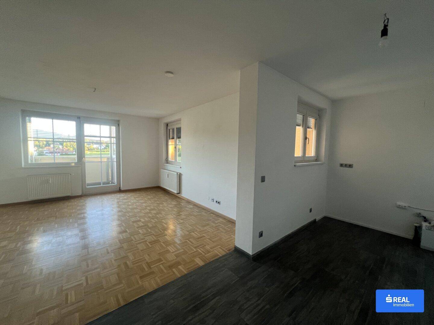Geräumiger Wohnbereich mit Parkettboden und Zugang zu einem kleinen Balkon.