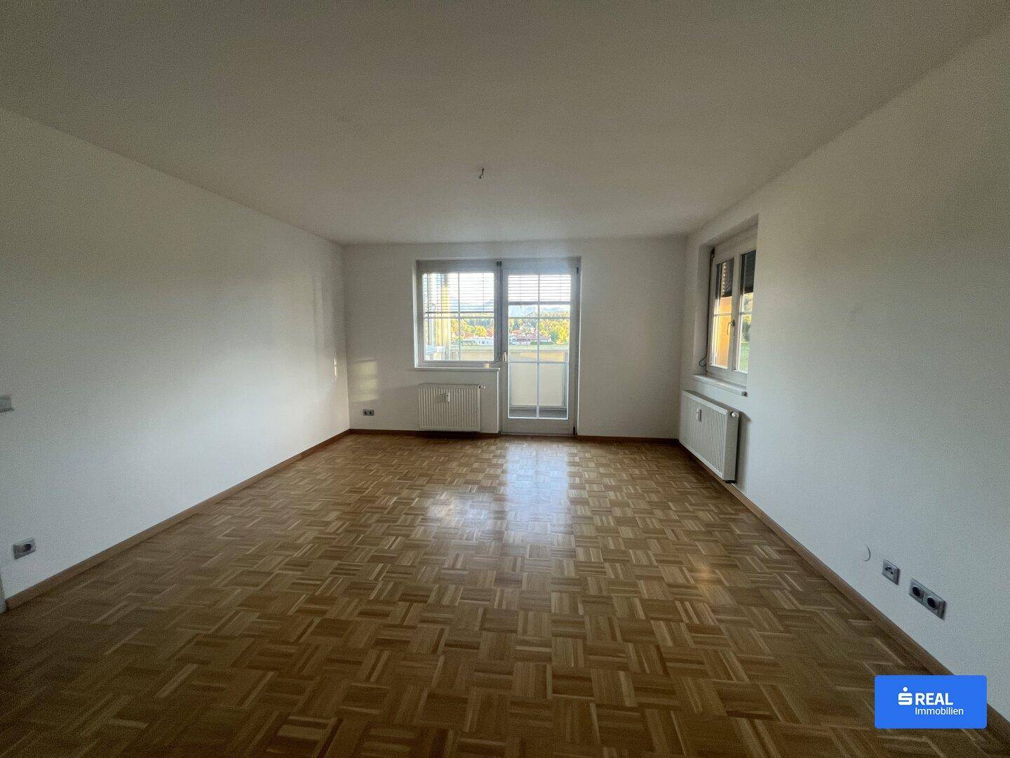 Heller und geräumiger Wohnbereich mit Parkettboden und Zugang zum Balkon.