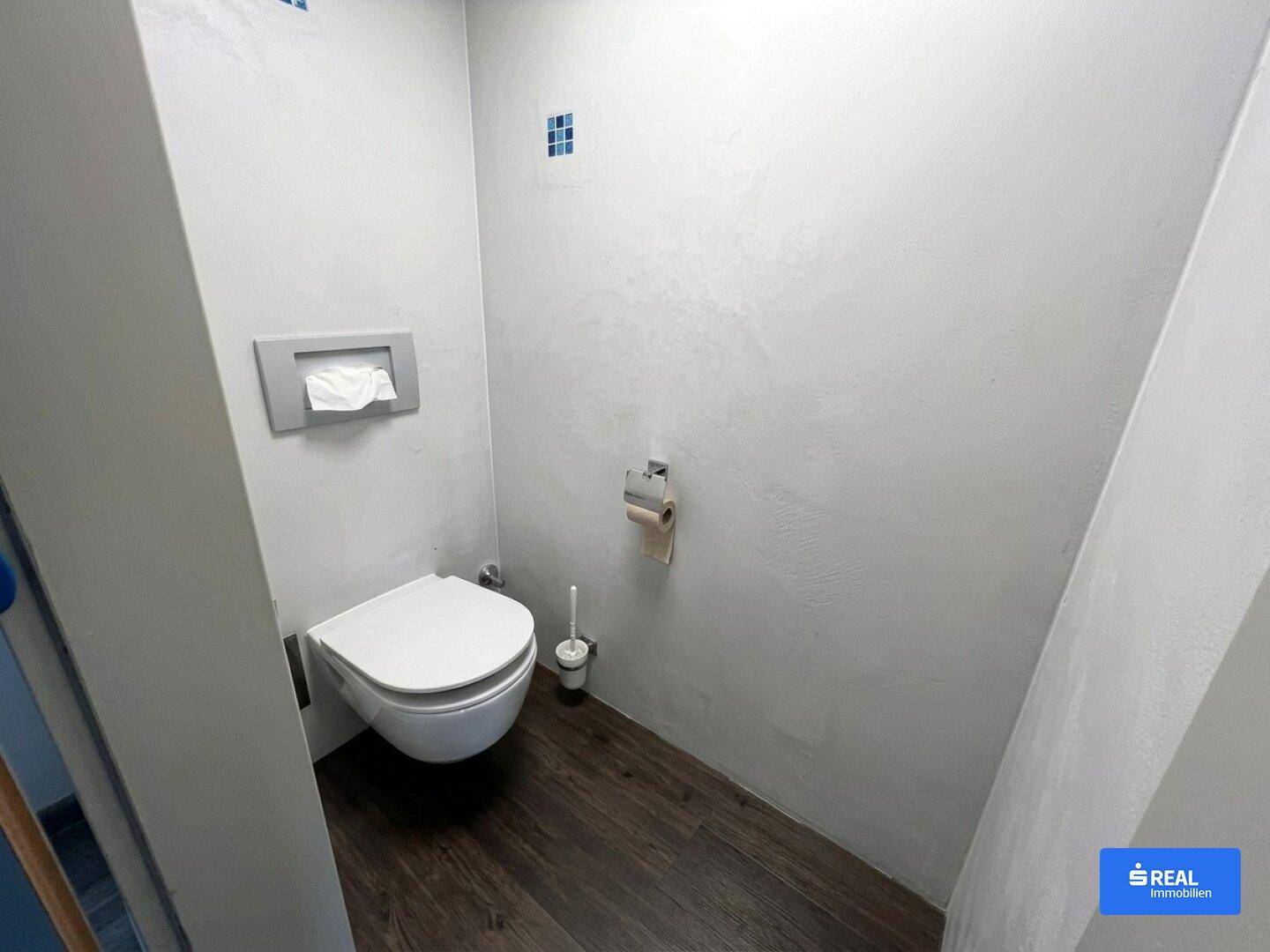 Modernes Gäste-WC mit wandhängender Toilette und dunklem Holzimitatboden.