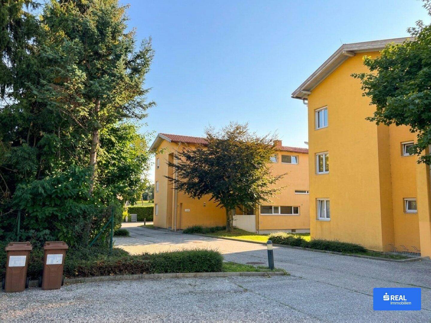 Gelbe Mehrfamilienhäuser mit Parkplätzen und grüner Umgebung an einem sonnigen Tag.