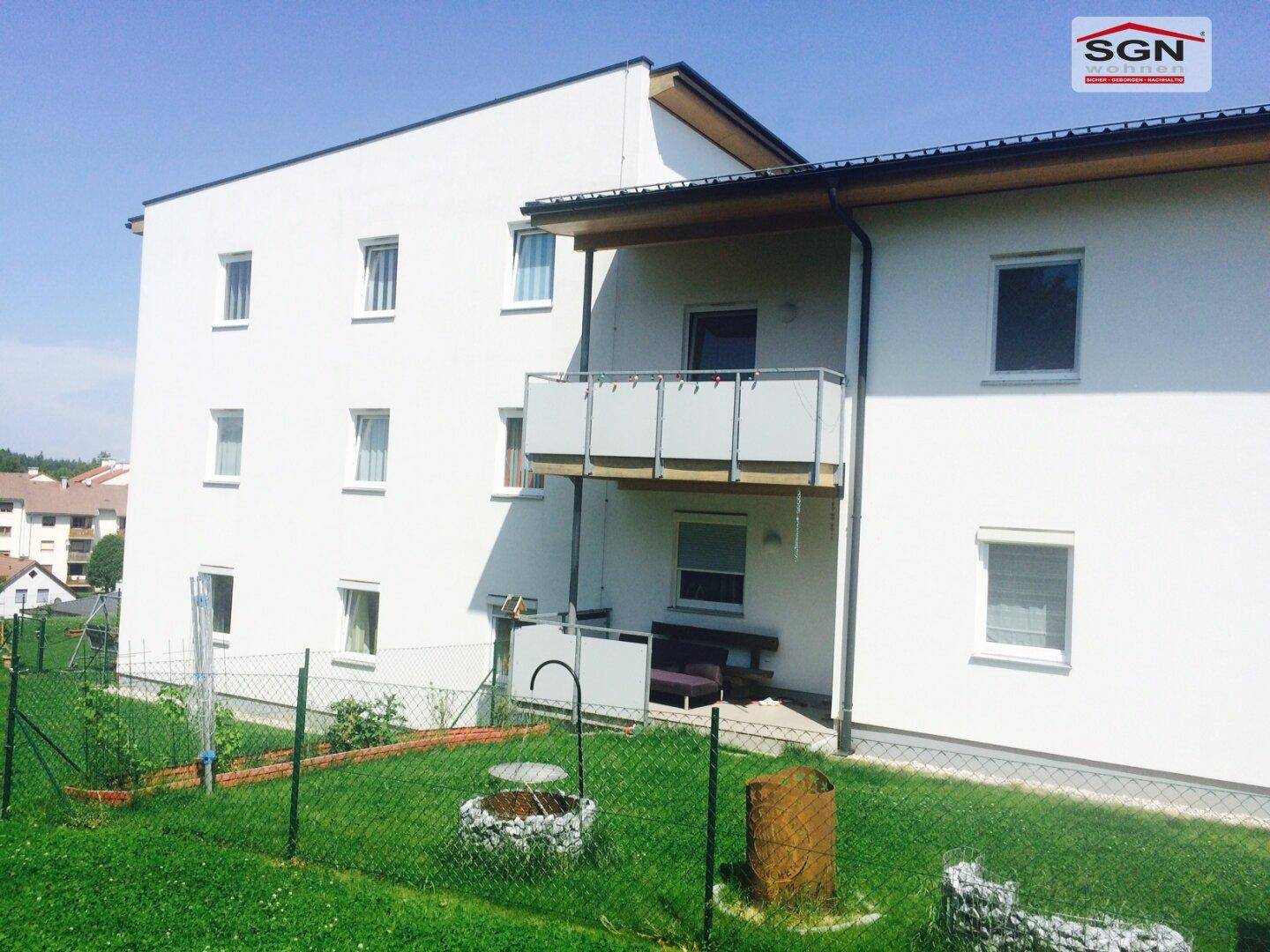 Weiße Gebäudefassade mit Balkon und Zugang zum Gartenbereich im Erdgeschoss.