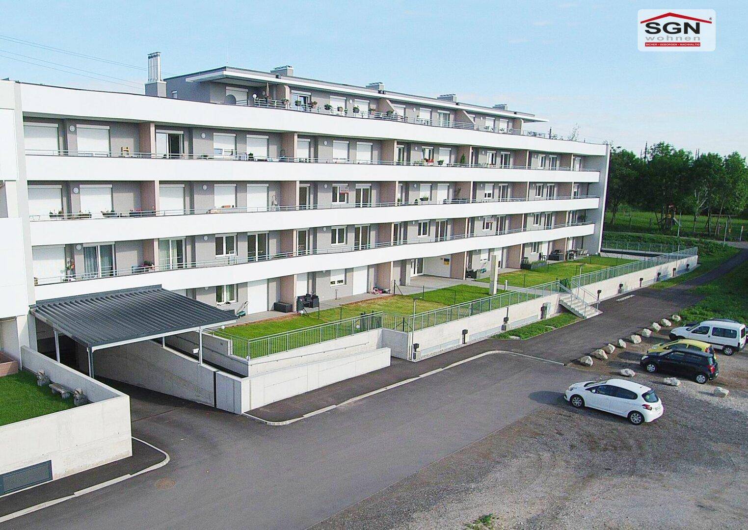 Gesamtansicht der modernen Wohnanlage mit Balkonen, Terrassen, Carport und Parkplätzen.