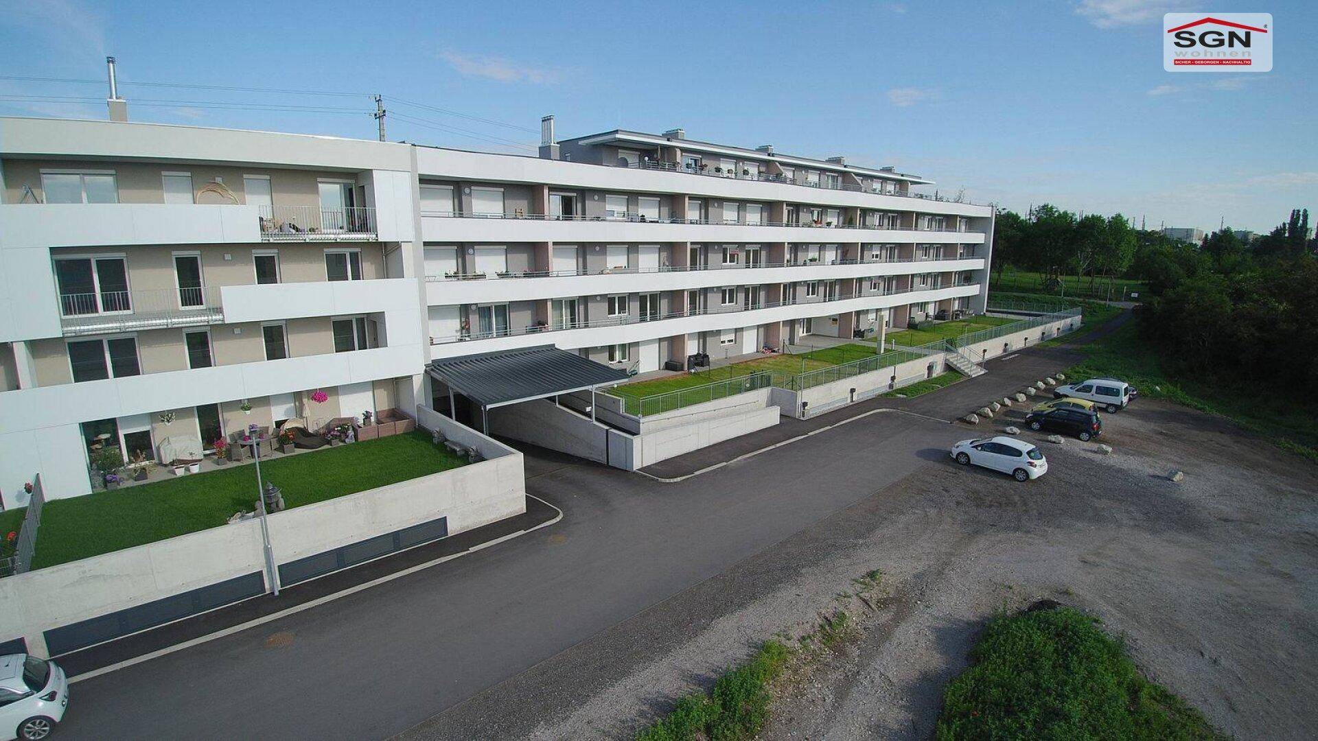 Luftaufnahme eines modernen Wohnkomplexes mit Balkonen, Grünflächen und Parkplätzen.