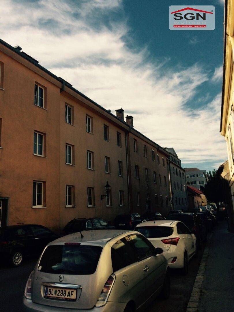 Lange Fassade eines Wohngebäudes entlang einer Straße mit parkenden Fahrzeugen.
