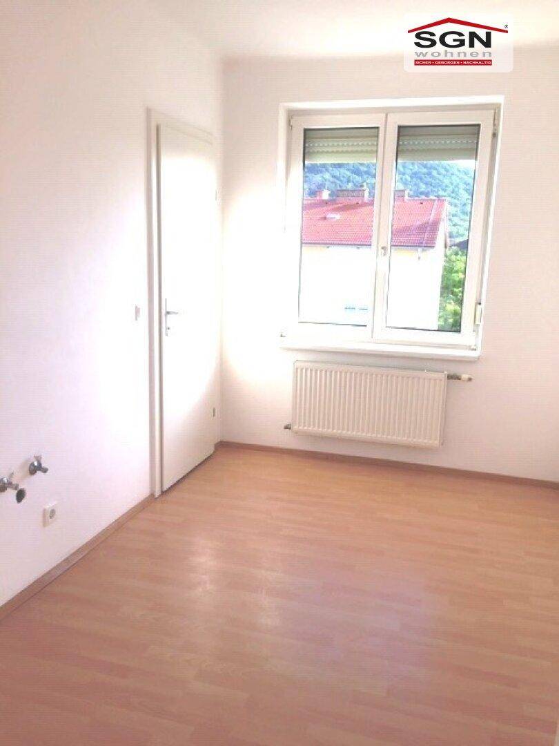Heller, leerer Raum mit Laminatboden, Fenster und Heizkörper, bereit zur individuellen Gestaltung.