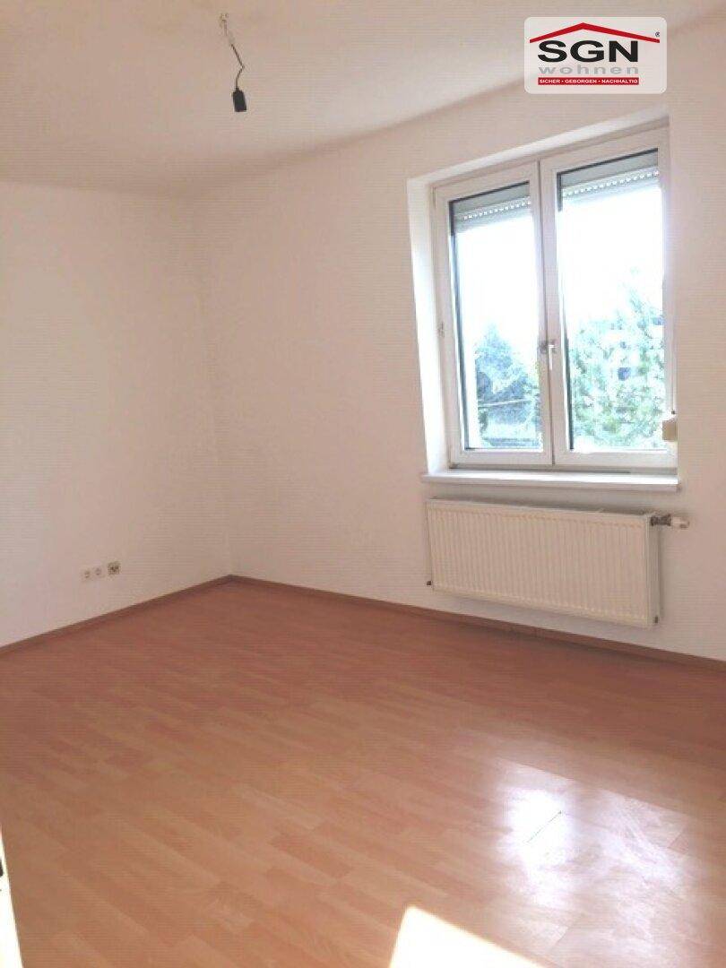 Leerer Raum mit hellem Laminatboden und Fenster, bietet viel Tageslicht für verschiedene Nutzungen.