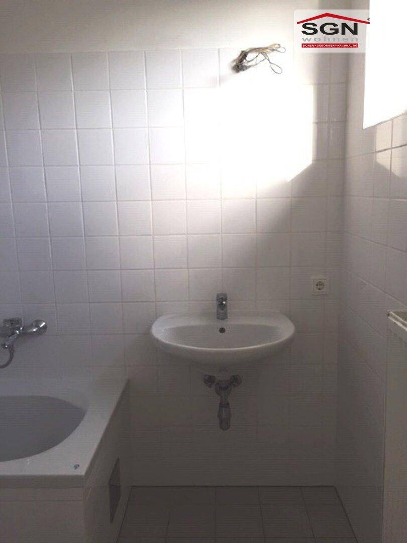 Helles Badezimmer mit Waschbecken und Badewanne, ausgestattet mit weißen Wandfliesen und Tageslicht.