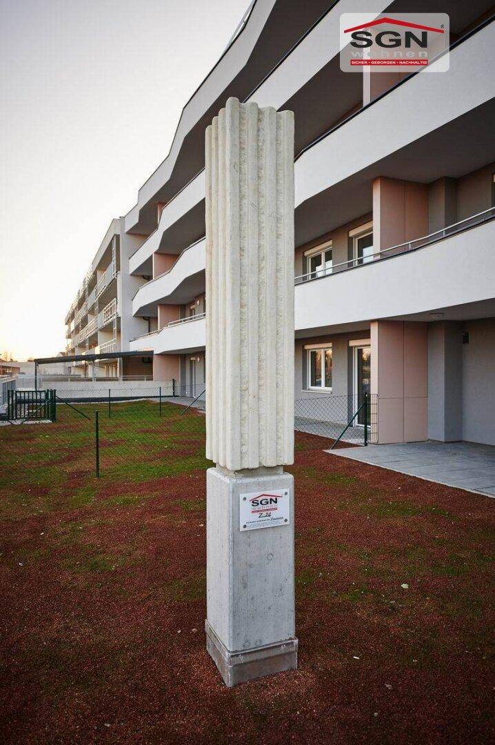 Moderne Wohnanlage mit Balkonen und Grünflächen, akzentuiert durch eine Skulptur im Vorgarten.