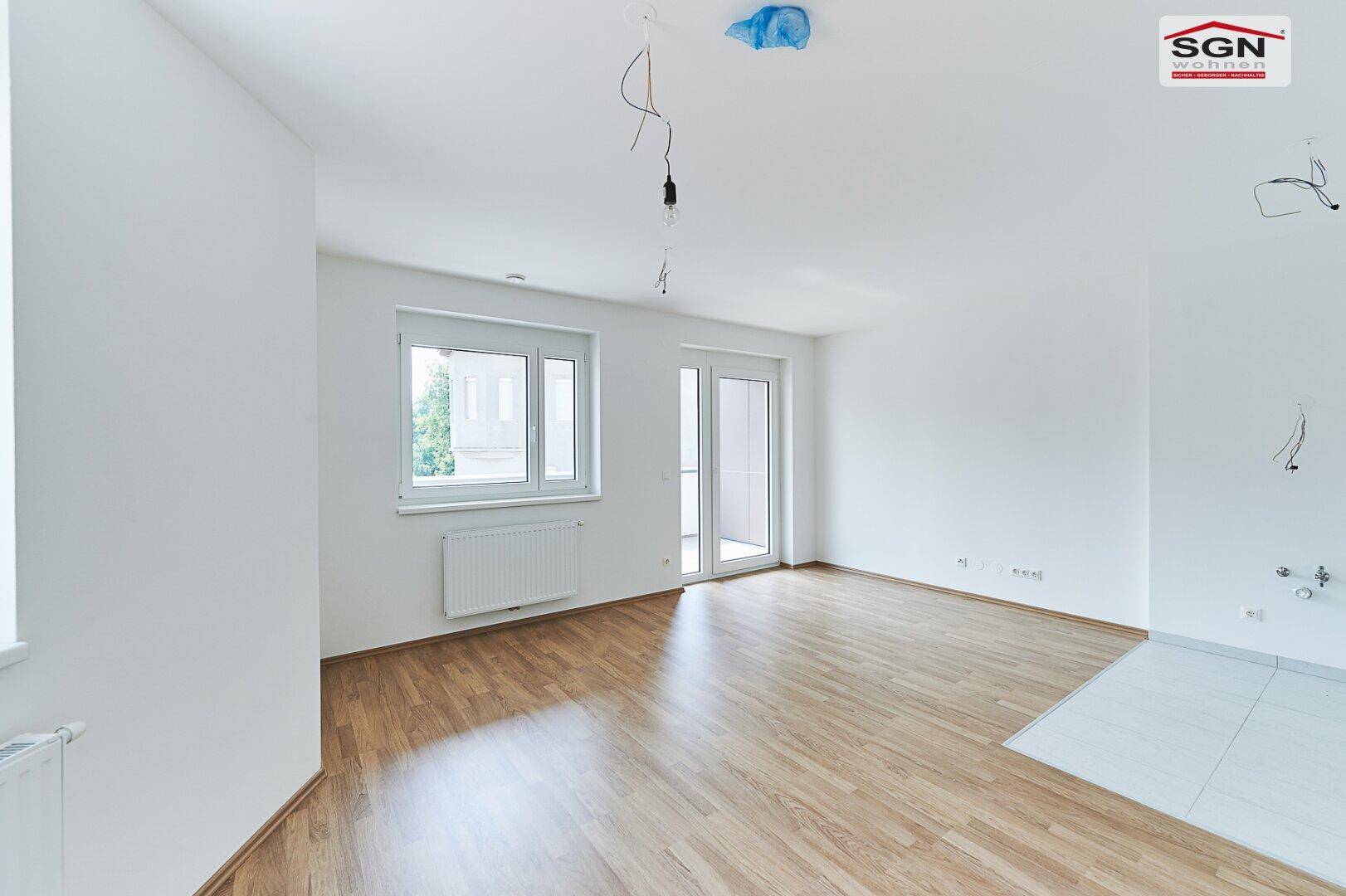Lichtdurchfluteter Wohnraum mit Holzboden, großem Fenster und Zugang zu einem Außenbereich.