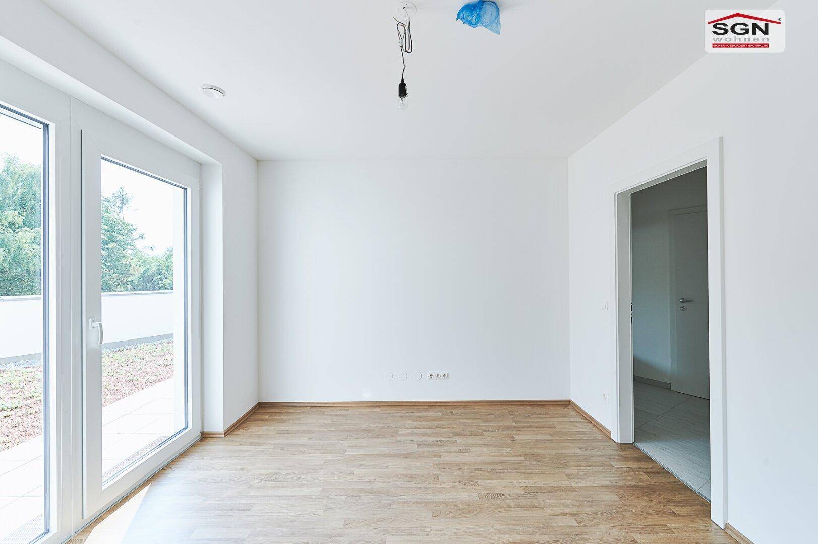 Heller Wohnraum mit Holzboden und großer Glastür, die zu einem Außenbereich führt.