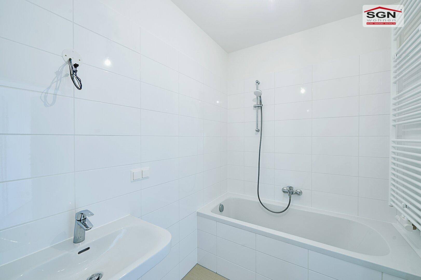 Modernes Badezimmer mit weißen Fliesen, Badewanne und Waschbecken in neuwertigem Zustand.