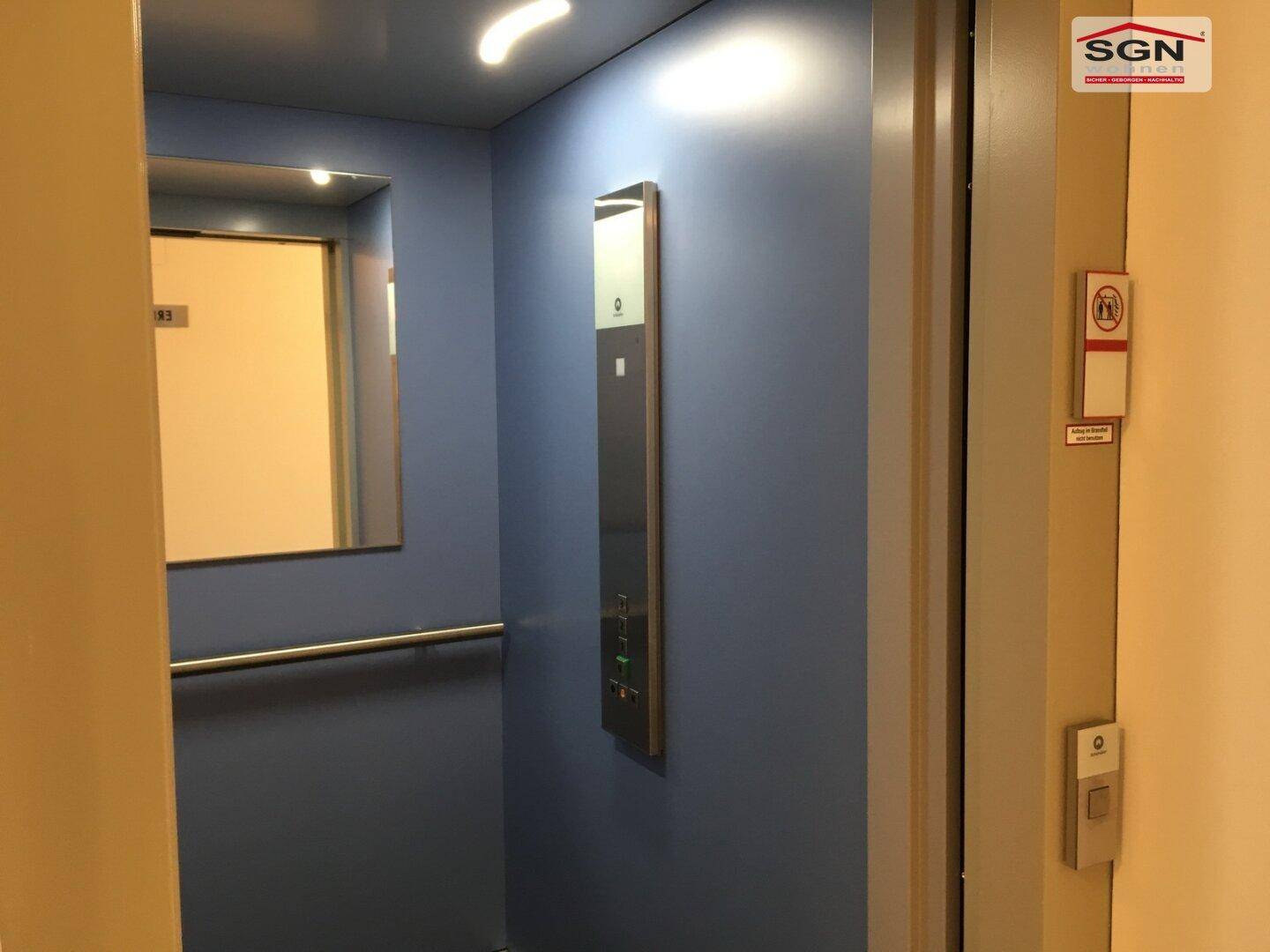 Moderner Aufzug mit blauen Wänden und Edelstahlbedienfeld im Gebäude.