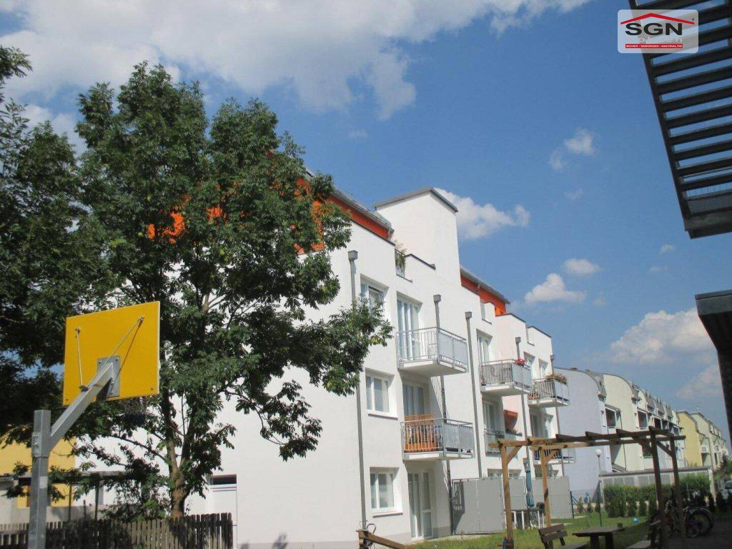 Ansicht eines modernen Wohngebäudes mit Balkonen und einem Basketballkorb im Außenbereich.