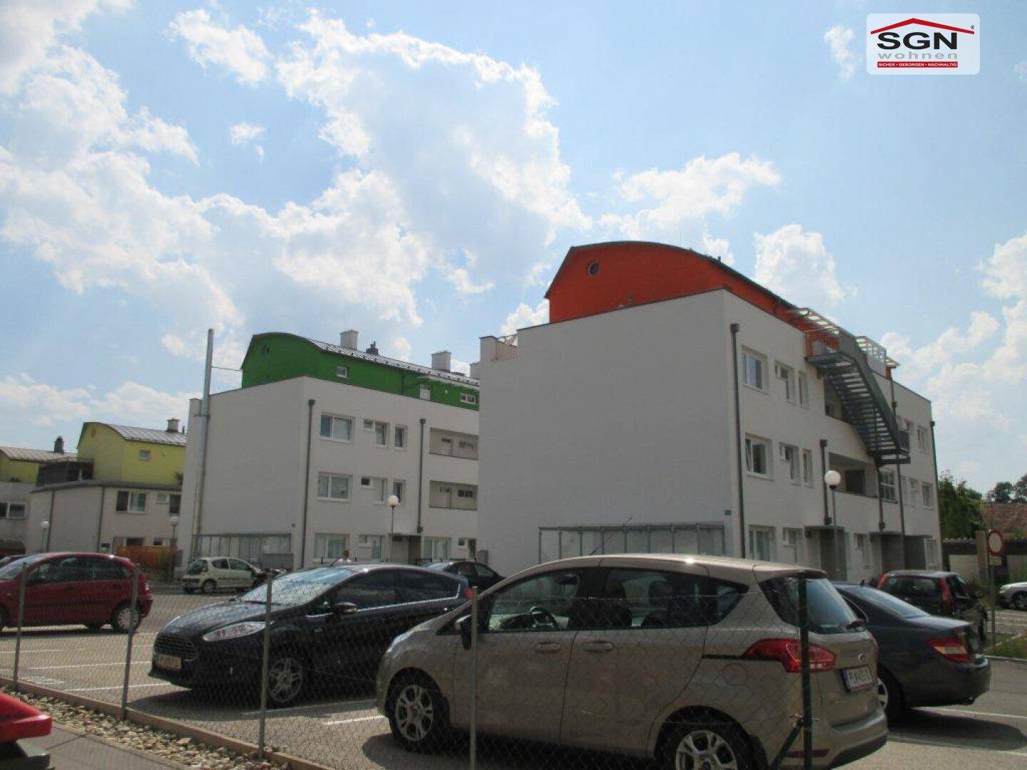 Mehrere moderne Wohngebäude mit unterschiedlichen Dachfarben und einem angrenzenden Parkplatz.