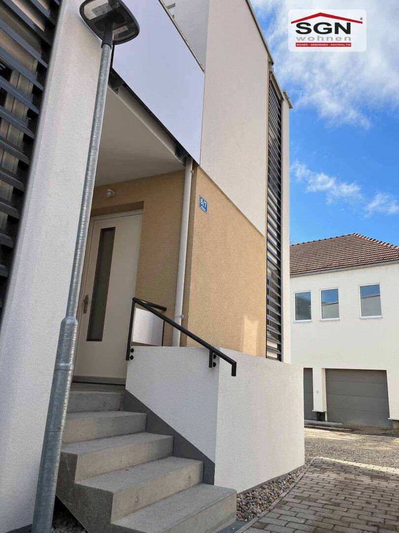 Eingangsbereich eines modernen Reihenhauses mit Treppe und heller Fassade unter klarem Himmel.