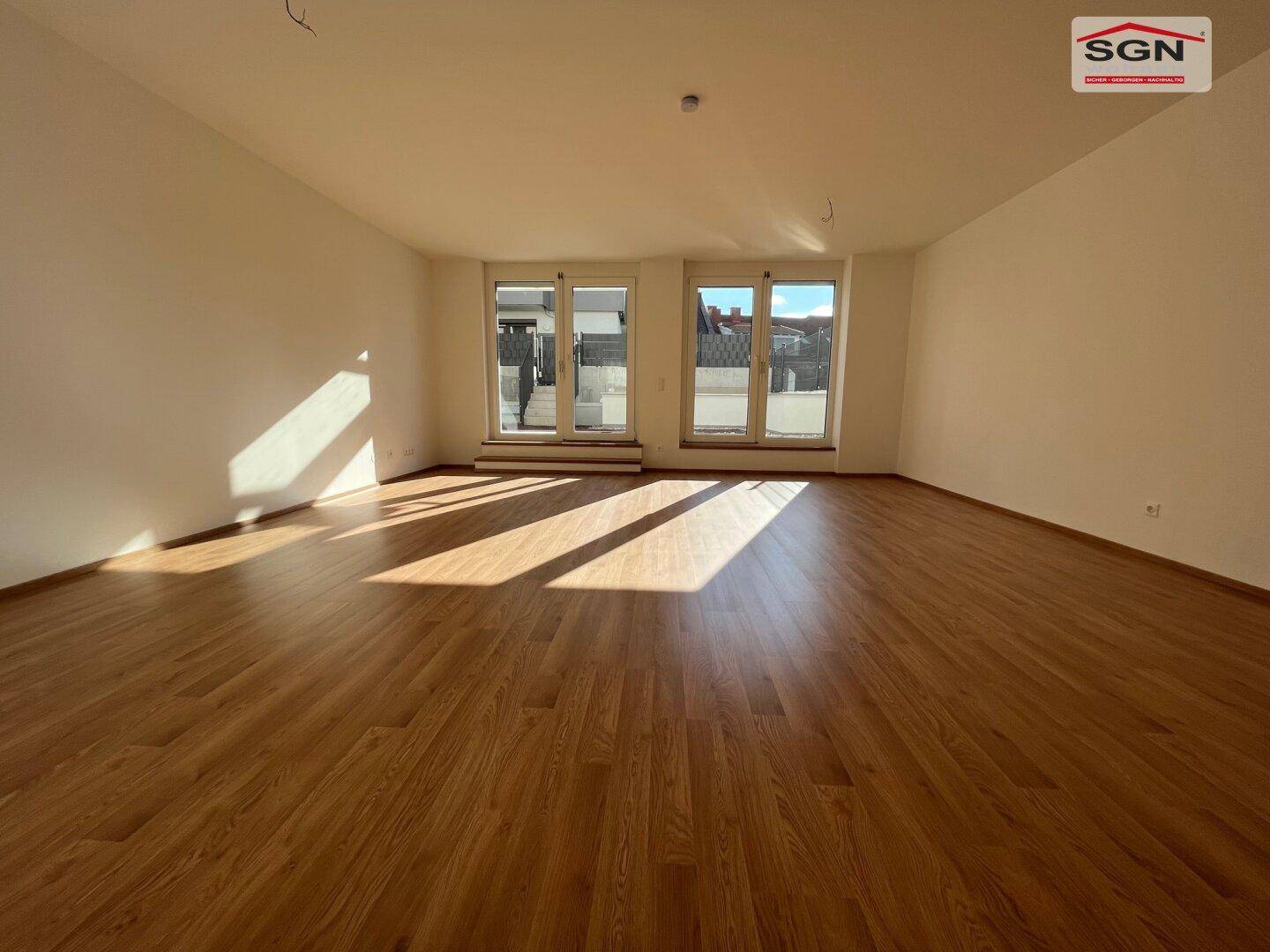 Helles, leeres Wohnzimmer mit neuem Laminatboden und großen Fenstern, die viel Tageslicht hereinlassen.