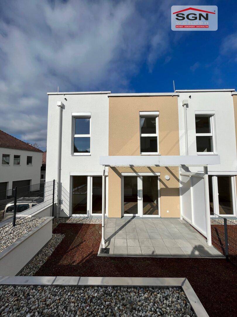 Private Terrasse mit angrenzendem Gartenbereich hinter einem modernen Reihenhaus, ideal für Entspannung.