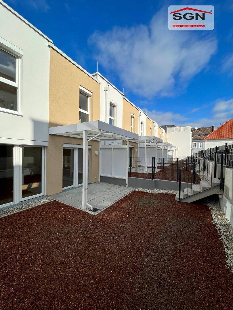 Reihe von Reihenhäusern mit privaten Terrassen und kleinen Gärten, die auf sonnige Tage warten.