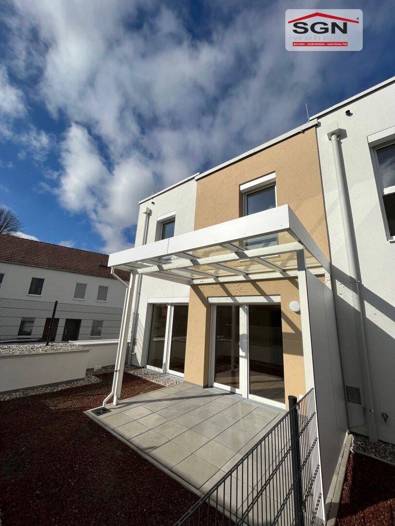 Einzelnes Reihenhaus von hinten mit überdachter Terrasse und Zugang zum kleinen Gartenbereich.