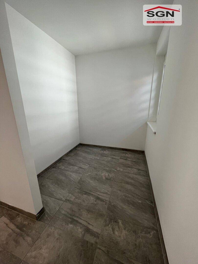 Kleiner, leerer Raum mit Fliesenboden und einem Fenster, ideal als Abstellraum oder Speisekammer.