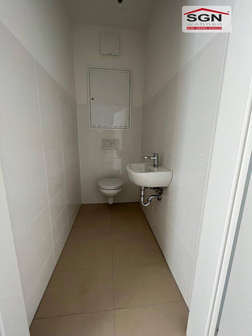 Modernes Gäste-WC mit weißen Fliesen, wandhängendem WC und kleinem Waschbecken.