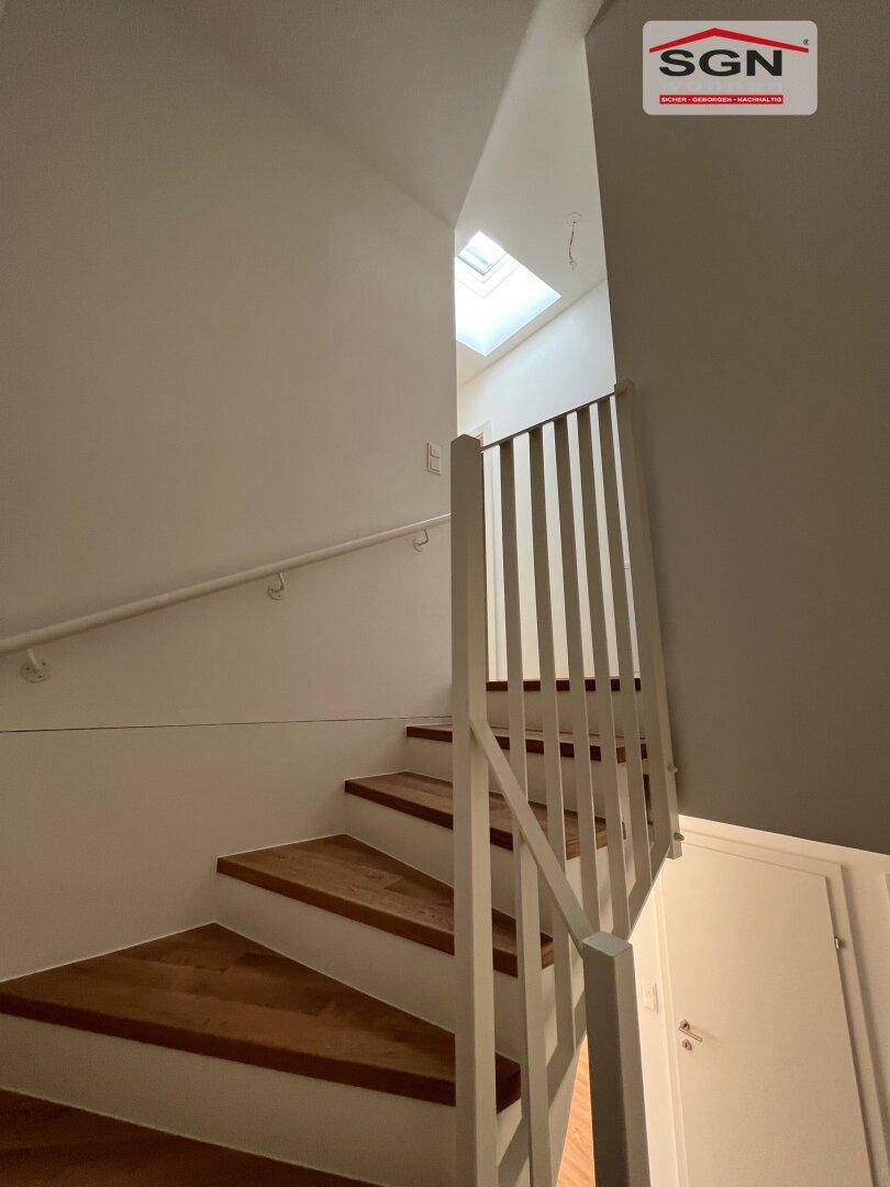 Heller Treppenaufgang mit Holzstufen und einem Oberlicht, das viel natürliches Licht spendet.