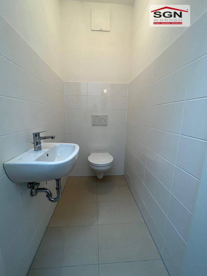 Modernes Gäste-WC mit wandhängendem WC, kleinem Waschbecken und weißen Fliesen an den Wänden.