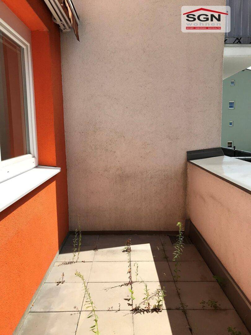 Kleiner, gefliester Balkon mit orangefarbener Wand und Blick auf die Umgebung.
