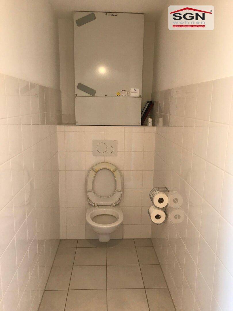 Separate Toilette mit weiß gefliesten Wänden und einem wandmontierten WC.