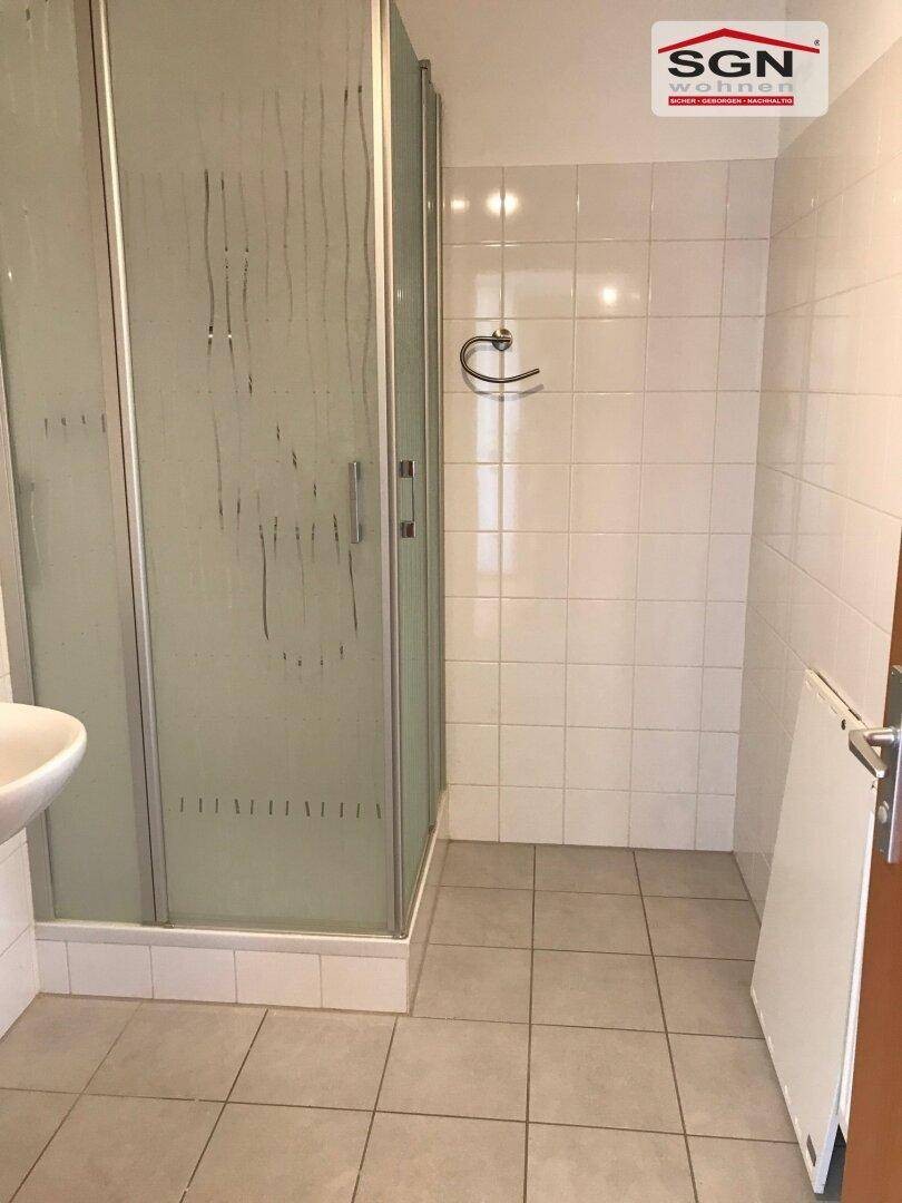 Badezimmer mit weiß gefliesten Wänden, Duschkabine und einem kleinen Waschbecken.