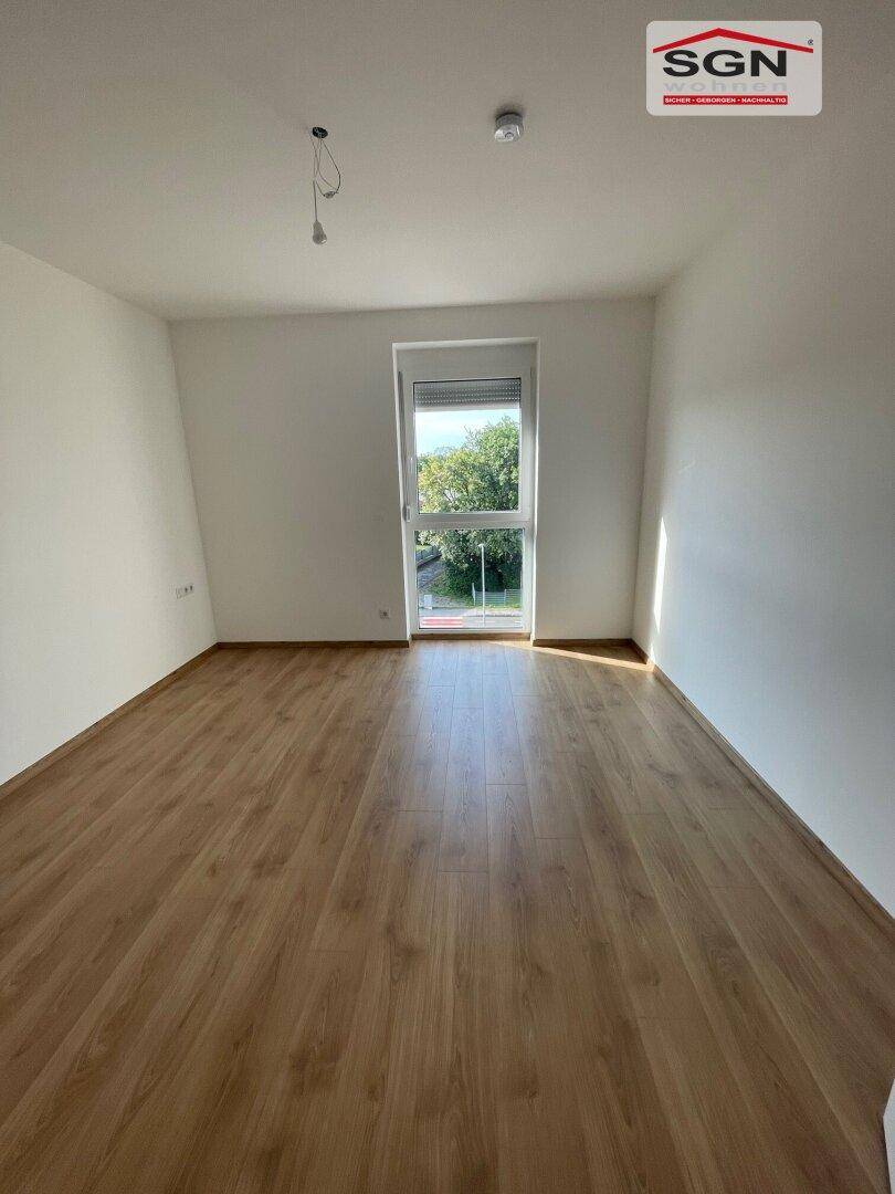 Helles Schlafzimmer mit Laminatboden und einem großen Fenster mit Blick ins Grüne.