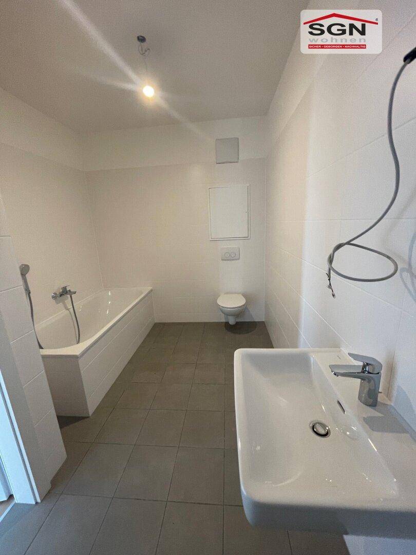 Modernes Badezimmer mit Badewanne, WC, Waschbecken und hellen Fliesen.