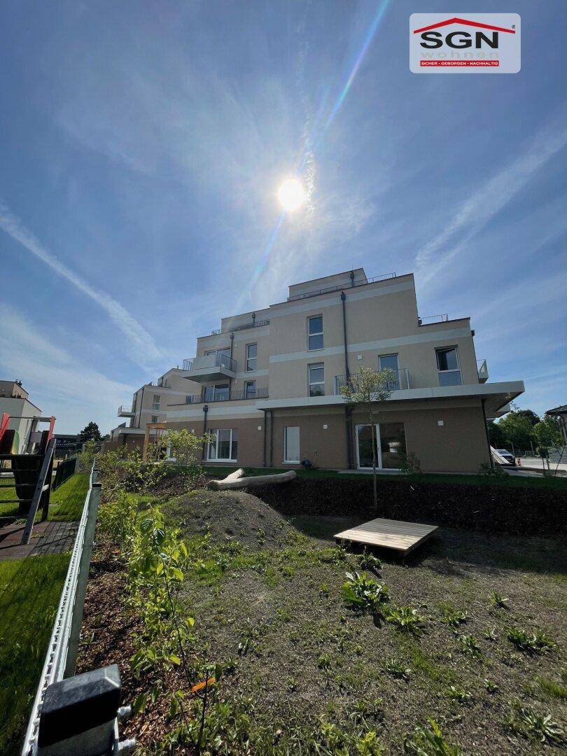 Neubau-Wohngebäude mit moderner Architektur, umgeben von Grünflächen und einem kleinen Spielbereich.