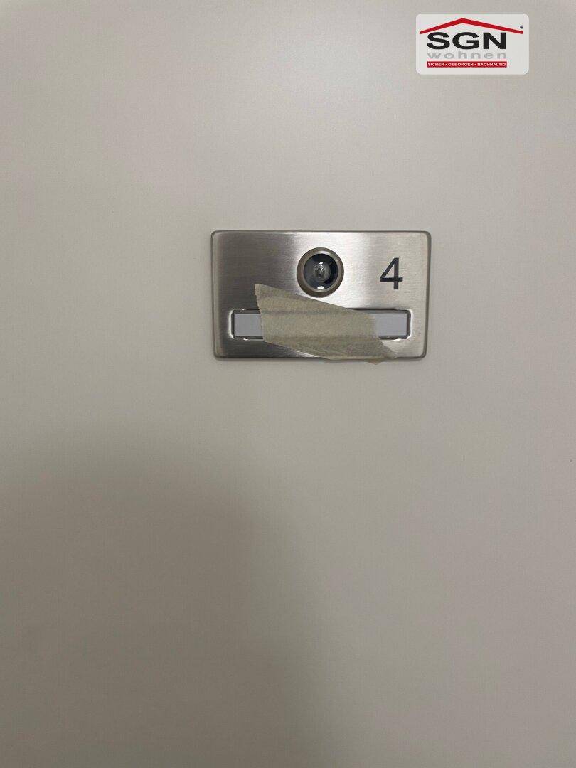 Detailaufnahme einer Wohnungstür mit Türspion und der Nummer vier.