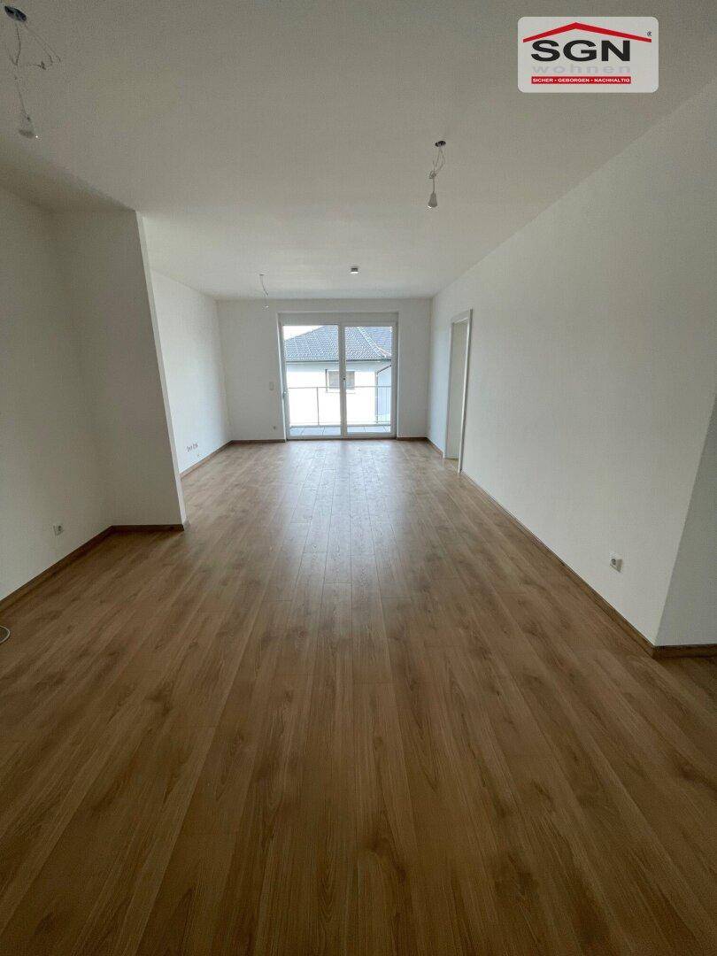 Helles, leeres Zimmer mit Laminatboden und Zugang zu einem Außenbereich durch eine große Glastür.