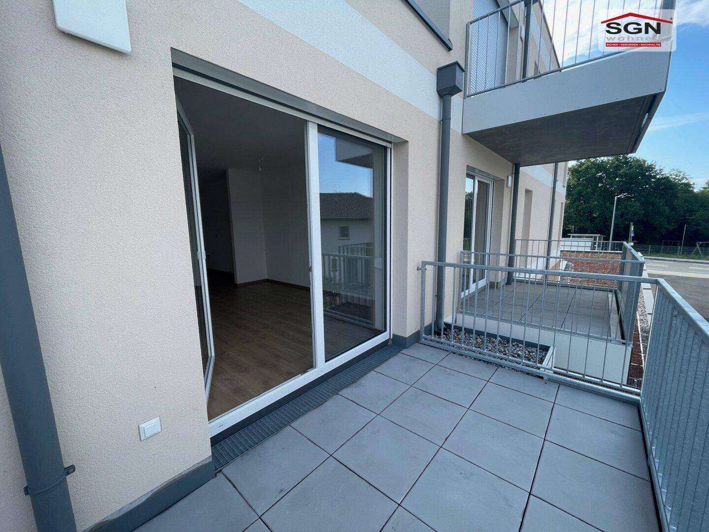 Balkon mit grauen Fliesen und Metallgeländer, mit Schiebetür zum Innenraum.