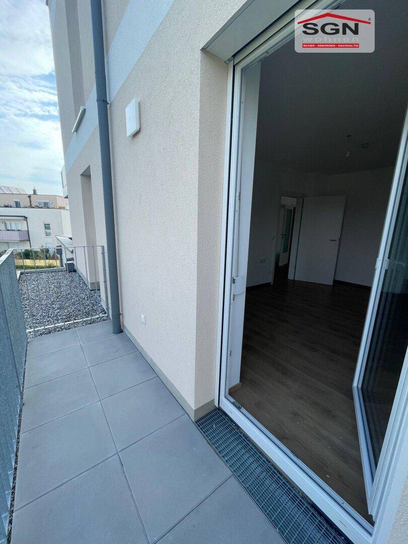 Balkon mit grauen Fliesen und Metallgeländer, mit Zugang zu einem hellen Innenraum.