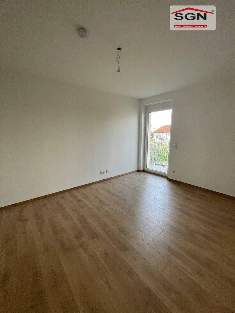 Helles Zimmer mit Laminatboden und einer Glastür, die zu einem französischen Balkon führt.