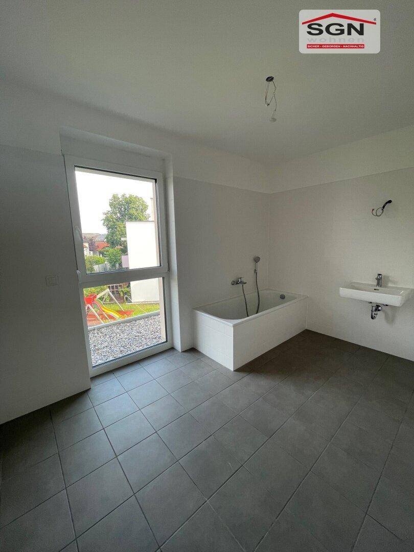 Modernes Badezimmer mit grauen Fliesen, Badewanne, Einzelwaschbecken und großem Fenster.