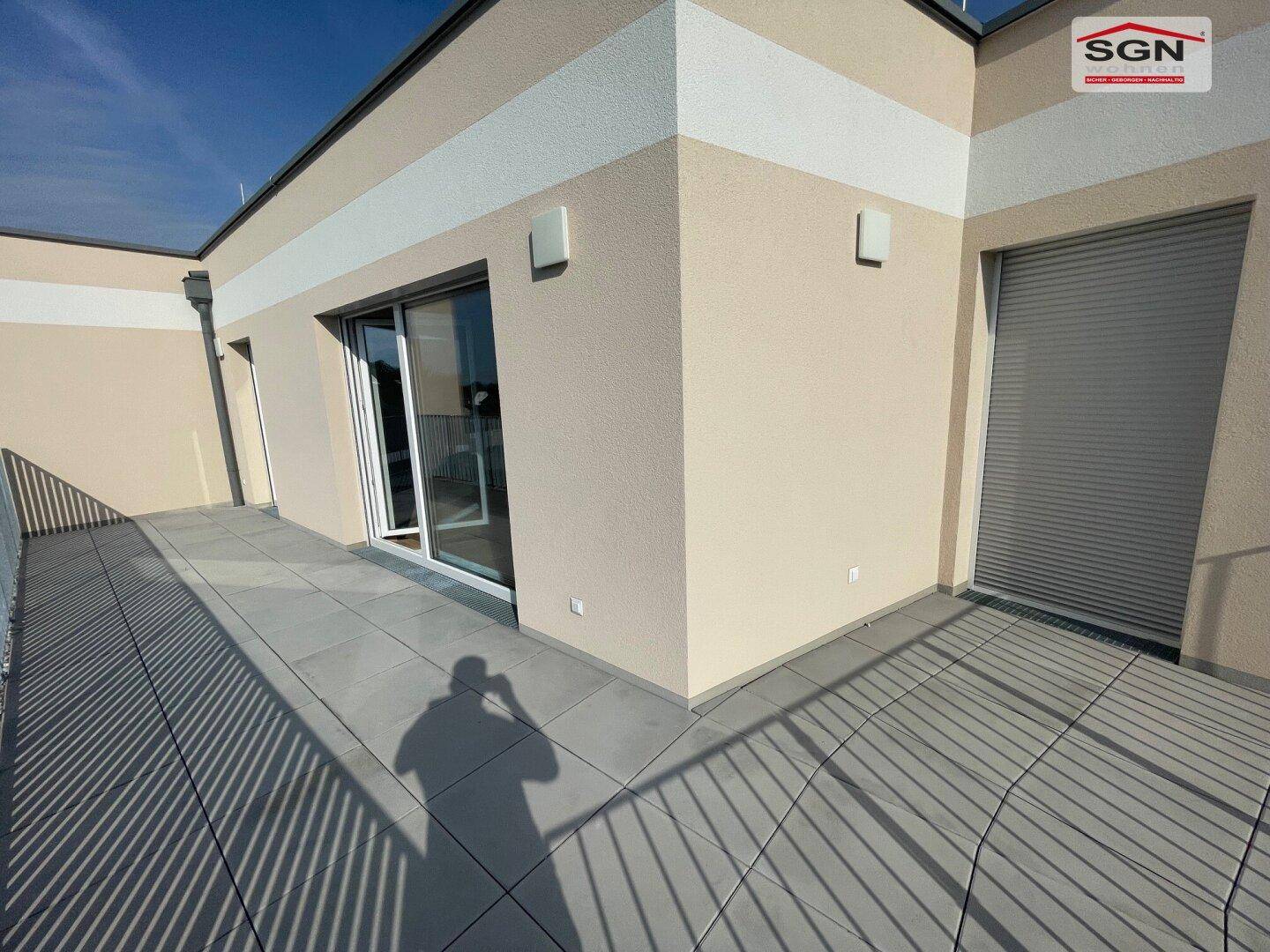 Geräumige Terrasse mit hellem Fliesenboden und Zugang zu den Innenräumen des Neubaus.