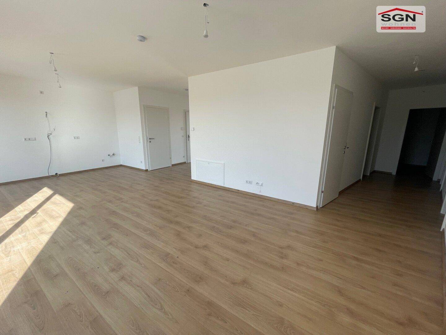 Heller, unmöblierter Wohnbereich mit neuem Laminatboden und weißen Wänden, bereit zum Einzug.