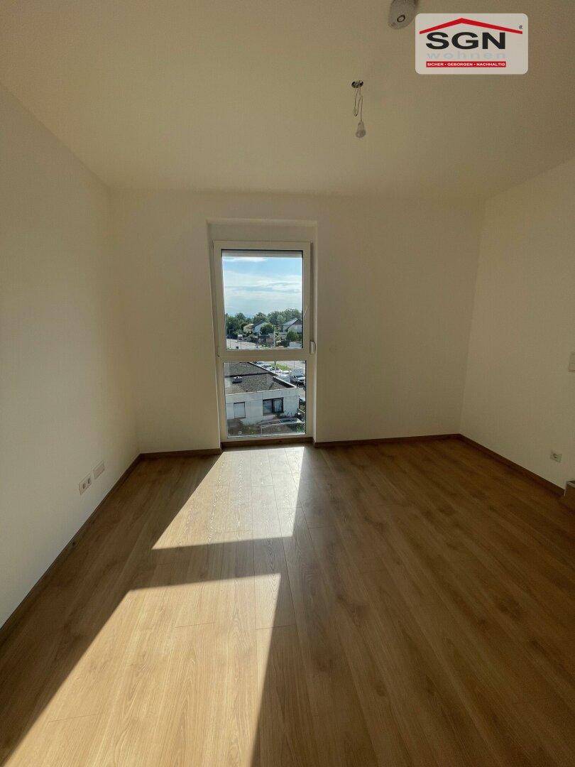Helles Schlafzimmer mit Laminatboden und einem großen Fenster, das viel Tageslicht bietet.