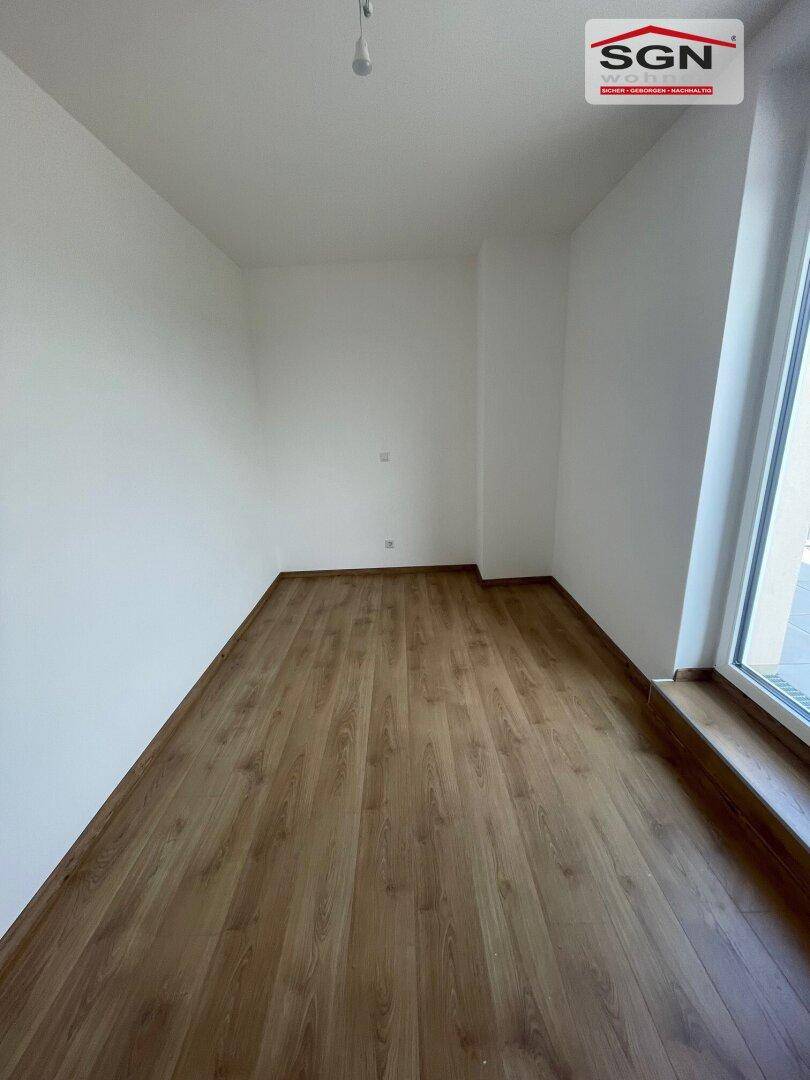 Weiteres helles Schlafzimmer mit Laminatboden und großem Fenster, das viel Licht spendet.