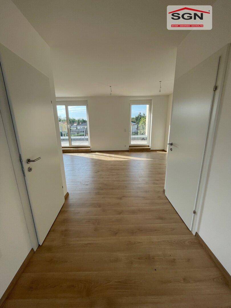 Lichtdurchfluteter Wohnbereich mit Laminatboden und großen Fenstern, die viel Tageslicht hereinlassen.