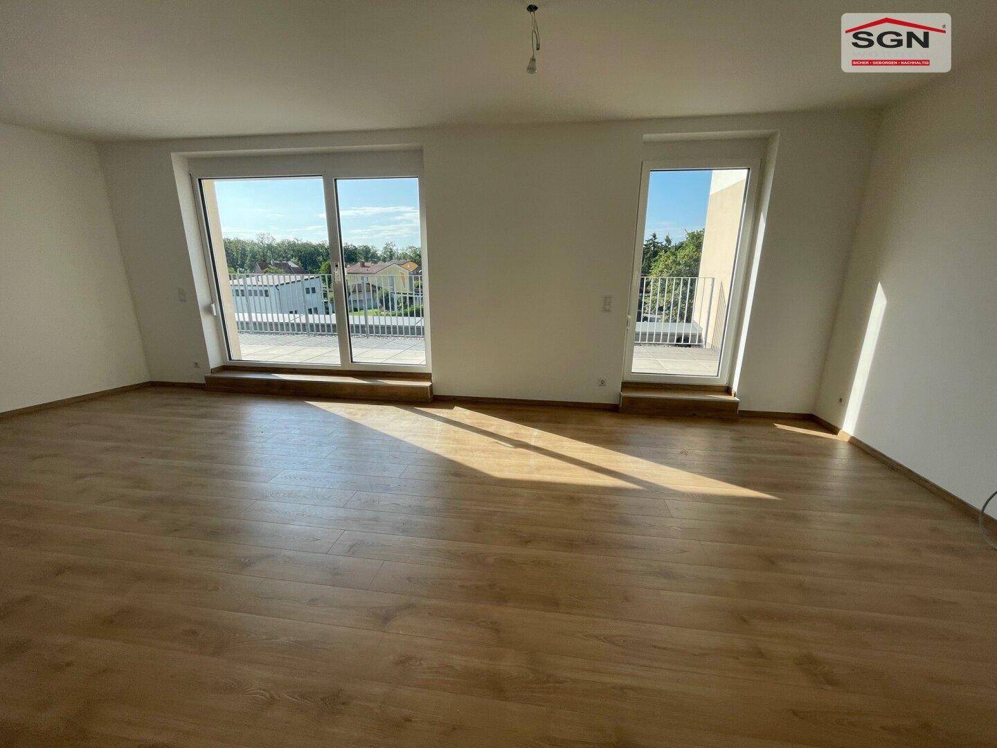 Geräumiger Wohnbereich mit hellem Laminatboden und Zugang zu einer sonnigen Außenterrasse.