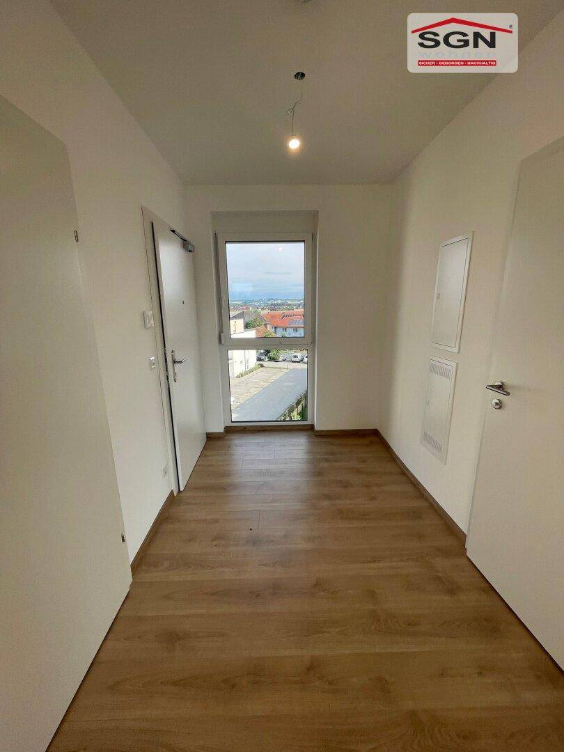 Heller Eingangsbereich mit Laminatboden und einer Tür, die zu den weiteren Räumen führt.