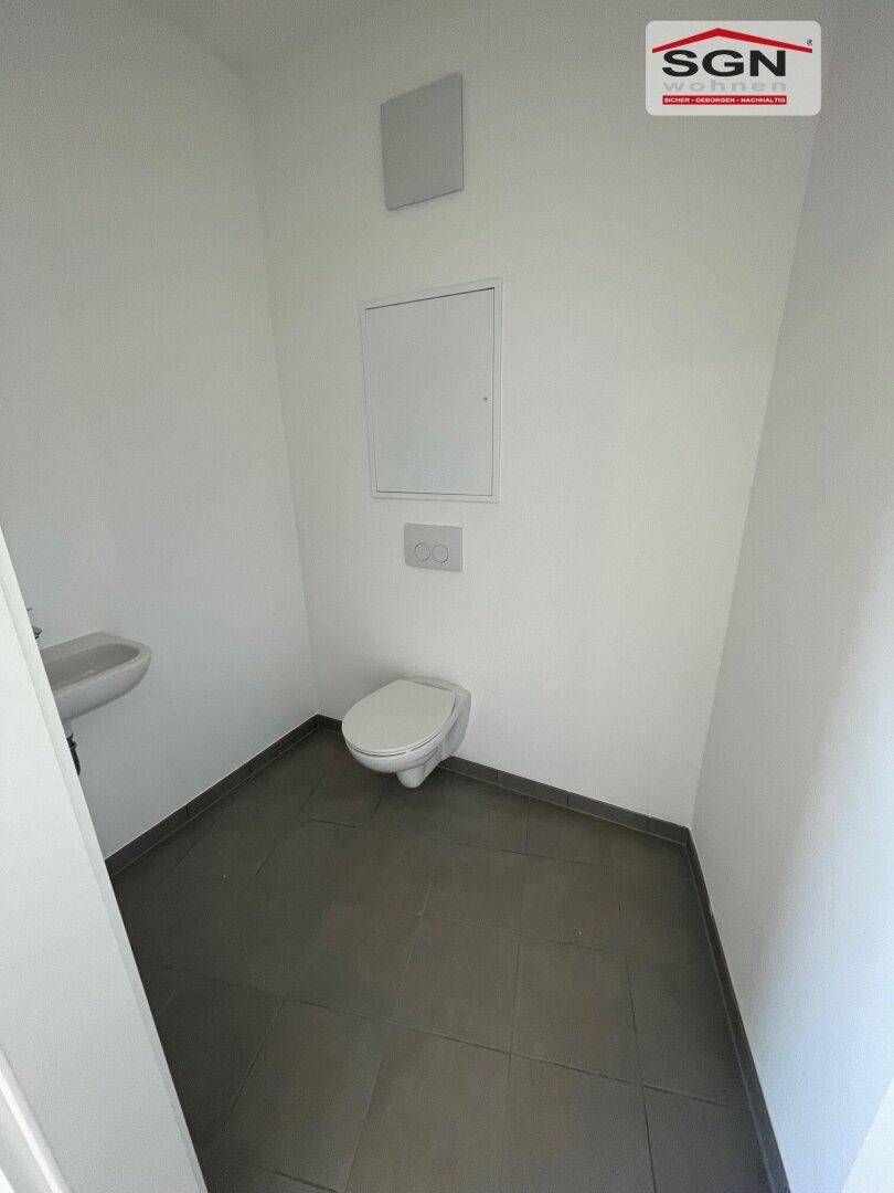 Modernes Gäste-WC mit Wand-WC, kleinem Waschbecken und dunklen Fliesen auf dem Boden.