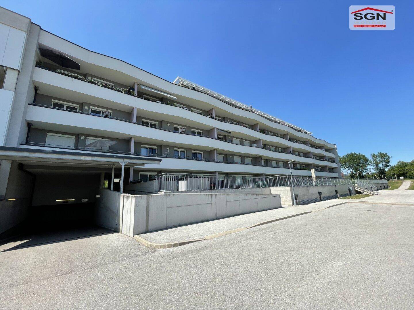 Modernes Wohngebäude mit Tiefgaragenzufahrt und Balkonen unter klarem Himmel.