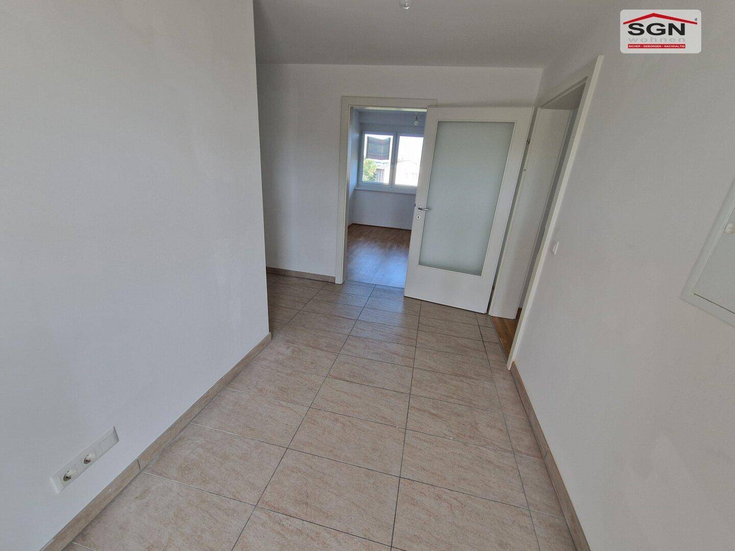 Flur mit hellen Fliesen und weiß gestrichenen Wänden, der zu weiteren Räumen führt.