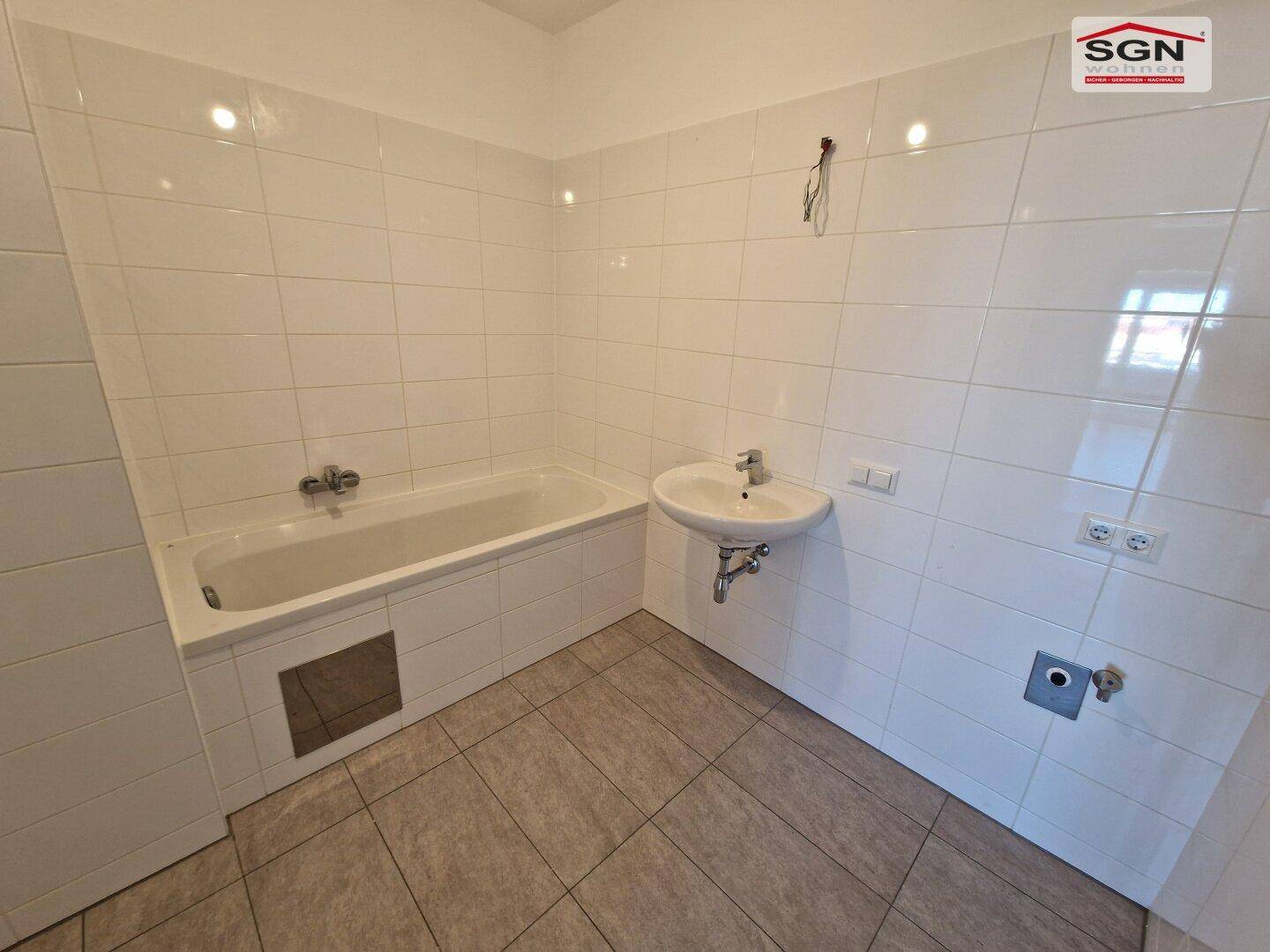 Badezimmer mit weißen Fliesen, Badewanne und Waschbecken, noch ohne Armaturen.